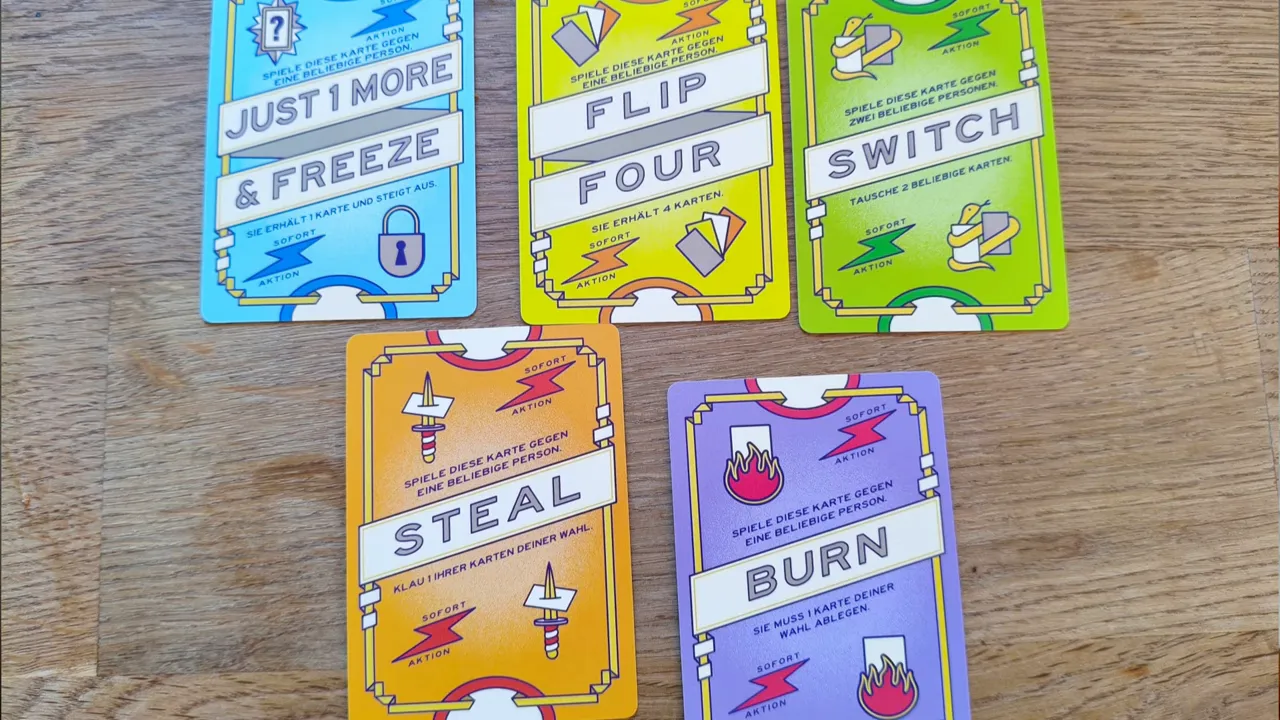 Fünf Aktionskarten mit den Aufschriften Just 1 More and Freeze, Flip Four, Switch, Steal und Burn auf einem Holztisch